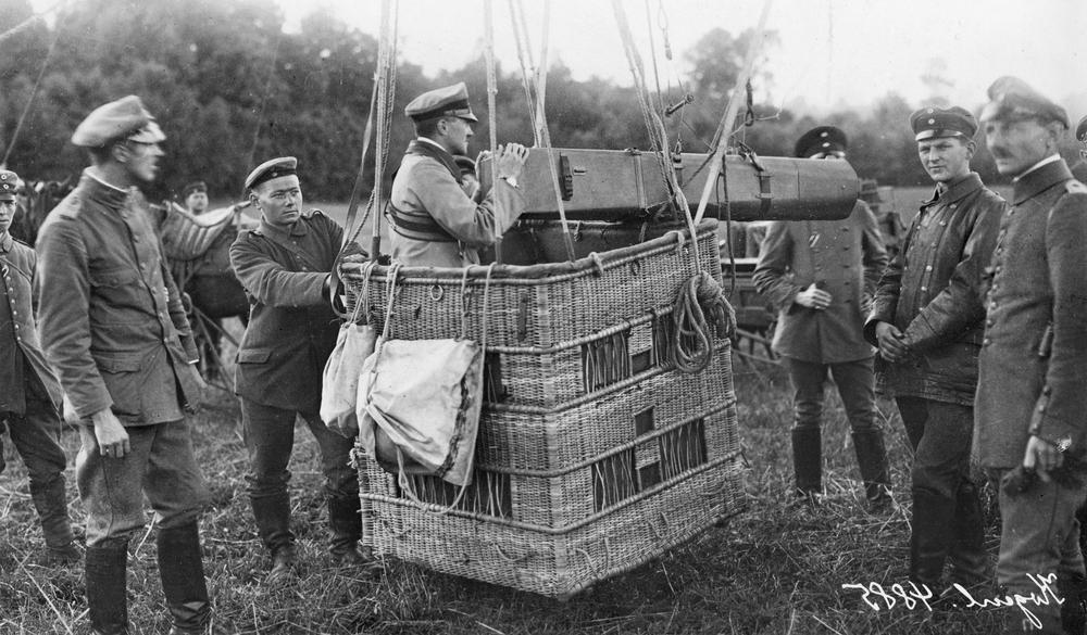 German observation balloon basket fitted with a long-distance camera and escape parachute, with ground crew preparing for ascent during World War I.