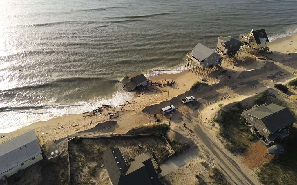 Aerial view of a collapsed beachfront house and scattered debris beside standing homes in Rodanthe, North Carolina.